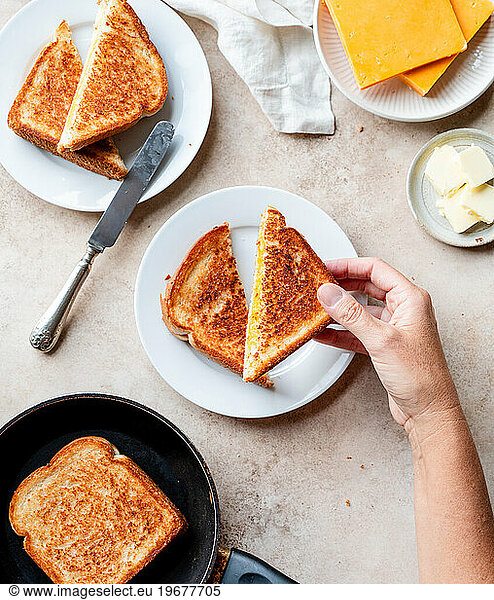Top view of hand picking up grilled cheese sandwich off plate.