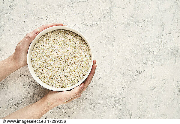 Top view of hands holding a bowl of raw white rice with copy space