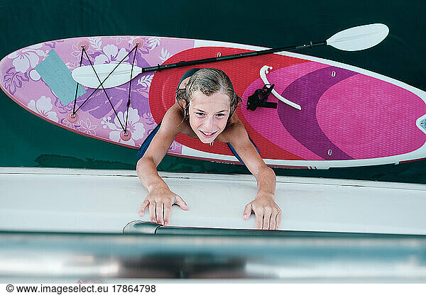 Top view of kid crawling on yacht from sup board.
