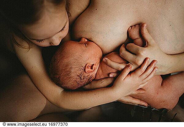 Top view of newborn baby breastfeeding and older sister hugging him