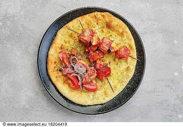 Top view of shashlik served on tortilla with tomato and red onion