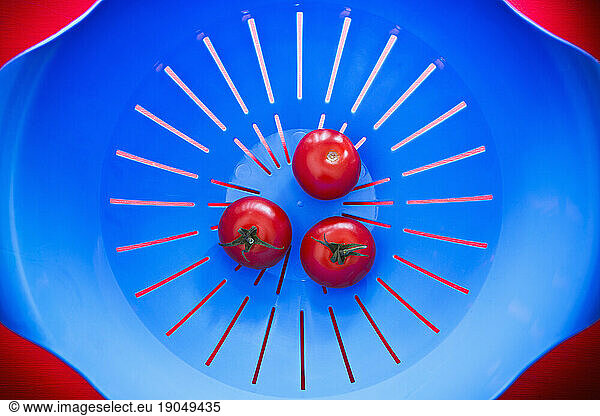 Top view of three tomatoes in a blue strainer