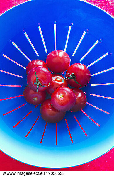 Top view of three tomatoes in a blue strainer