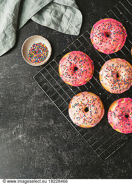 Top view of vanilla cake donuts with pink icing and sprinkles on rack.