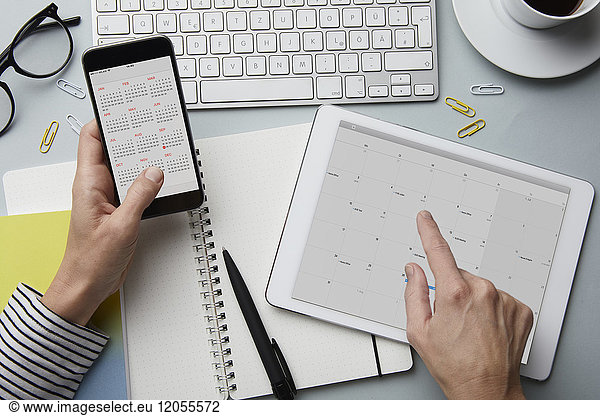 Top view of woman holding smartphone and tablet with calendar on desk