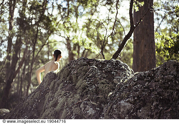 Topless figure stands behind rocks in forrest