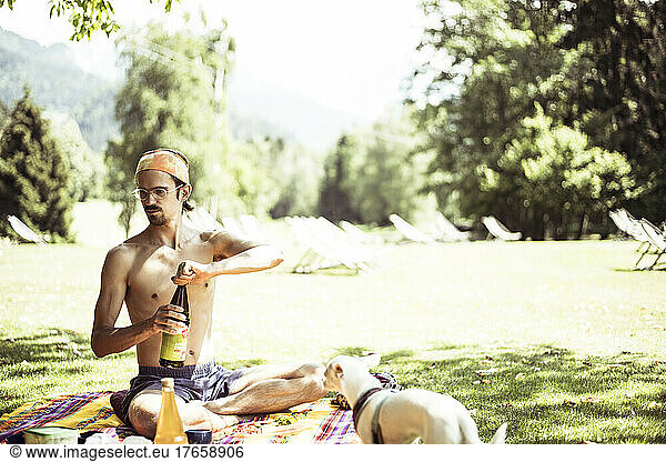 topless natural man opens bottle at summer picnic with small dog