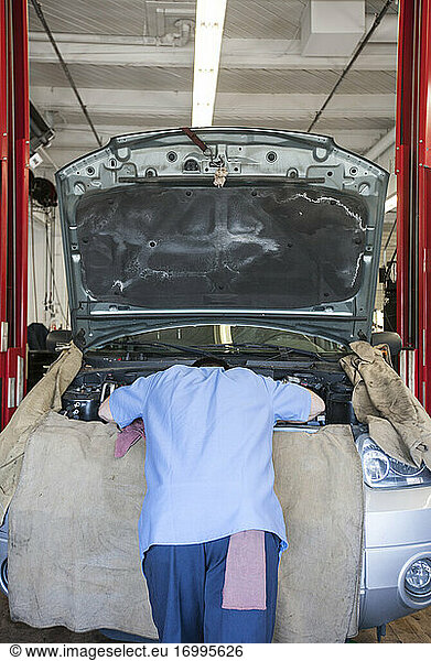 Torso of a mechanic leaning into the engine compartment in an auto repair shop