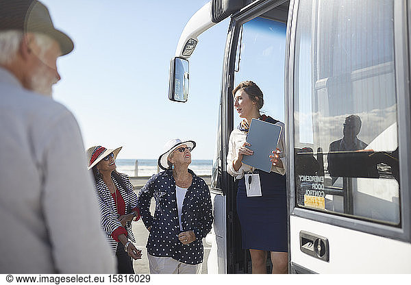 Tour guide talking to active senior tourists at doorway of tour bus
