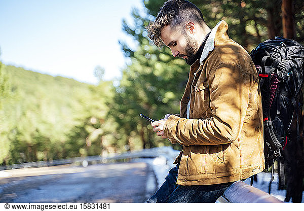 Tourist in den Bergen beim Autostopp mit seinem Handy