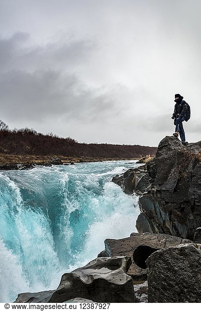Tourist  junger Mann steht an einem Wasserfall am blauen Fluss Brúará  Südisland  Island  Europa