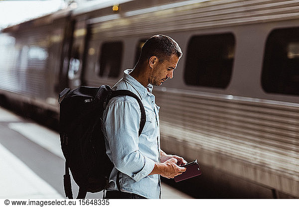 Tourist with backpack using smart phone on railroad station platform