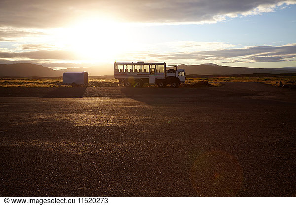 Touristen-Lkw bei Sonnenaufgang in einer Landschaft mit fernen Bergen geparkt  Island