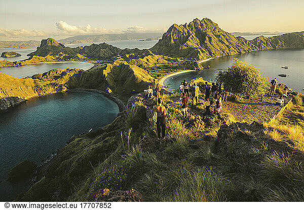 Tourists enjoy a viewpoint over a rugged coastline  looking out to the landforms and ocean at sunset  Komodo National Park; East Nusa Tenggara  Indonesia