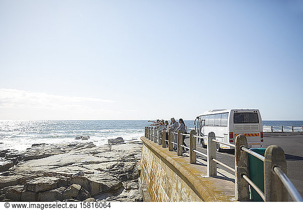 Tourists looking at sunny ocean view outside tour bus