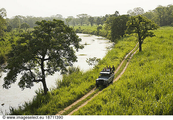 Tourists on a wildlife safari ride in the back of a jeep down a dirt road through Royal Chitwan National Park  Nepal.