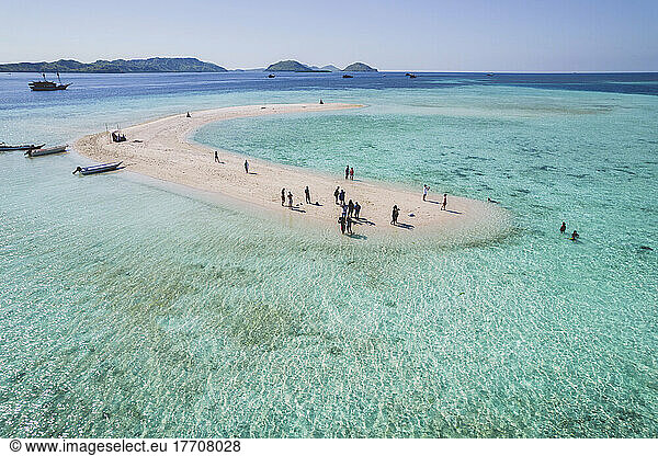 Tourists stand on a white sand atoll surrounded by clear turquoise coloured water  small motorboats pulled into shore  Komodo National Park; East Nusa Tenggara  Indonesia