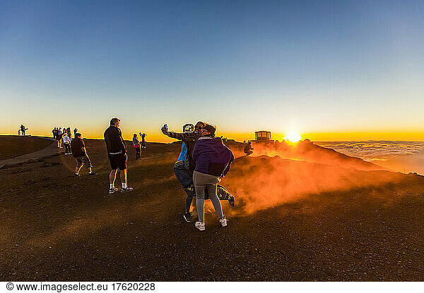 Tourists take photographs and view the Haleakala Observatory buildings above the clouds during a colourful  dramatic sunset; Maui  Hawaii  United States of America