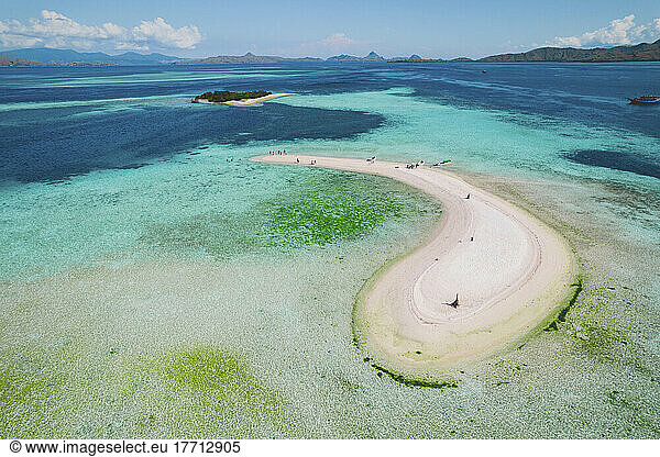 Tourists walk on a white sand atoll surrounded by clear turquoise coloured water  some swimming in the water  Komodo National Park; East Nusa Tenggara  Indonesia