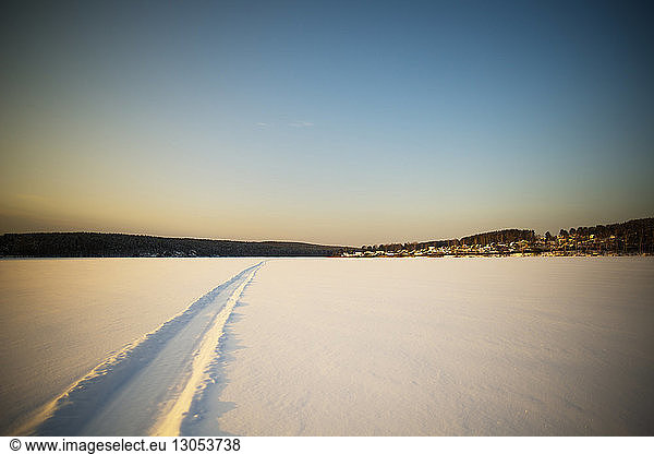 Track on snow covered field against clear sky