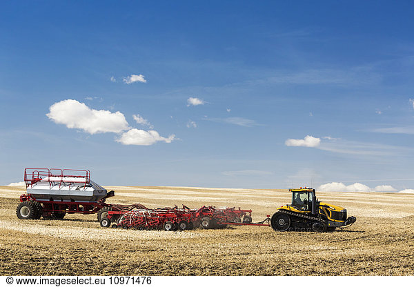 Tractor and air seeder in stubble field planting crop with blue sky and clouds; Alberta  Canada