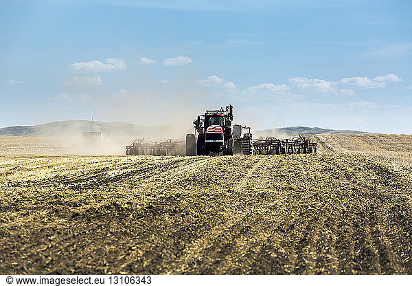 Tractor pulling an air seeder seeding a field with blue sky and clouds in the background; Rockyford Alberta Canada