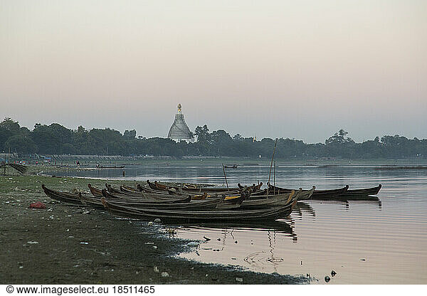 Traditional boats line up on the shore at sunset on a lake in Myanmar.