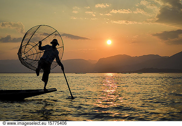 Traditional fisherman balancing on one leg on a boat  holding fishing basket  fishing on Lake Inle at sunset  Myanmar.