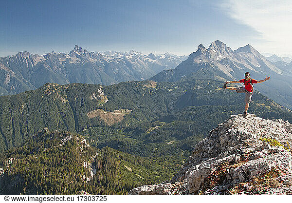 Trail runner balances and stretches on a mountain summit.