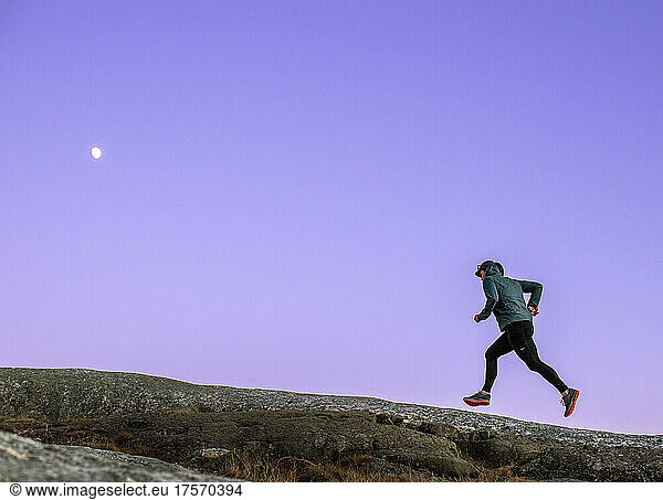 Trail runner climbs mountain with purple sky and moon