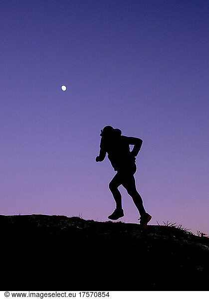 Trail runner silouhetted against purple sky at twilight with moon