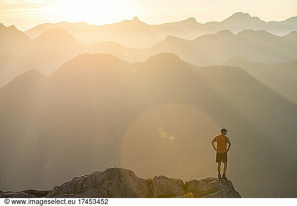Trail runner standing on edge of a mountain cliff at sunset.