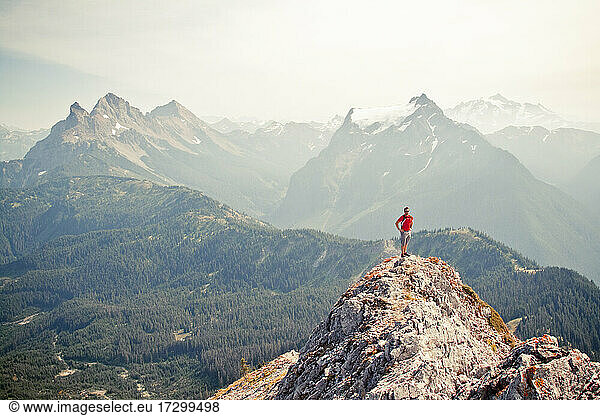 Trail runner stands on the airy summit of a rocky mountain ridge.