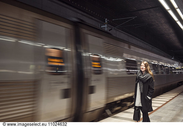 Train passing by woman standing at subway station