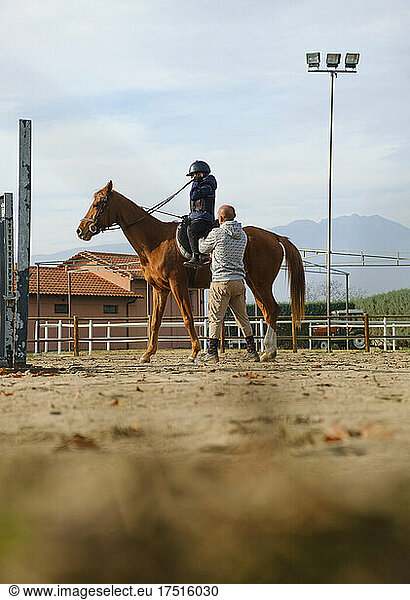 Trainer teaching kid horse back riding with obstacles.