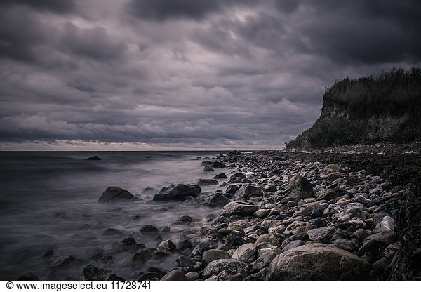Tranquil rocks on ocean beach below stormy  overcast clouds  Bisserup  Denmark