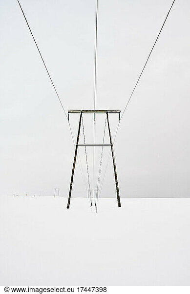Transmission tower with wires above snowy terrain in winter
