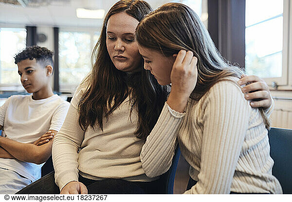 Trauriges Teenager-Mädchen  das den Arm um eine Freundin legt und sie in einer Gruppentherapie tröstet