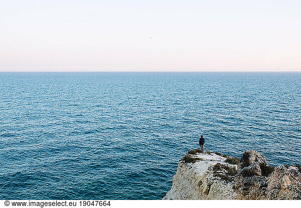 Traveler in a hat stands on a rock against a beautiful sea with waves