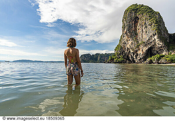 Traveler woman in turquoise water looking towards the Phra nang Cave.