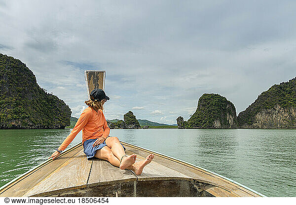 Traveler woman sitting in typical Thai boat admiring mountain scenery