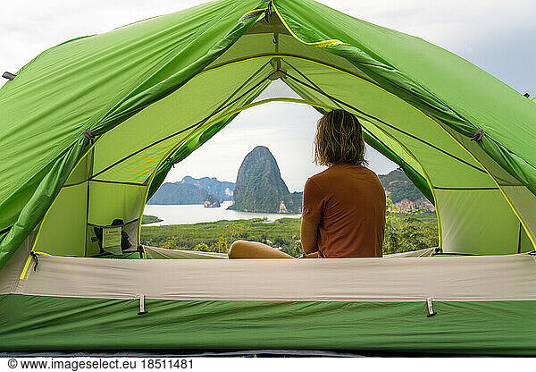 Traveler woman sitting inside tent admiring scenery of Phang Nga Bay