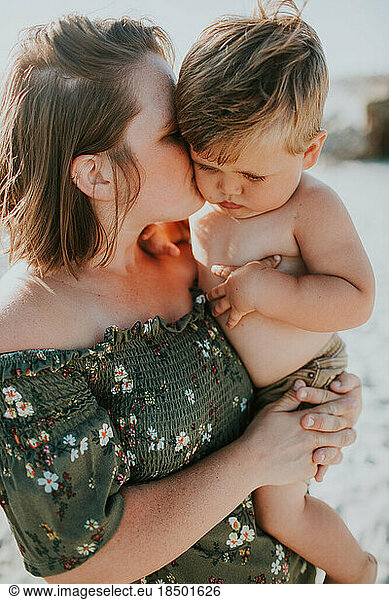 Trendy dressed young mom kissing chubby cheeks of toddler