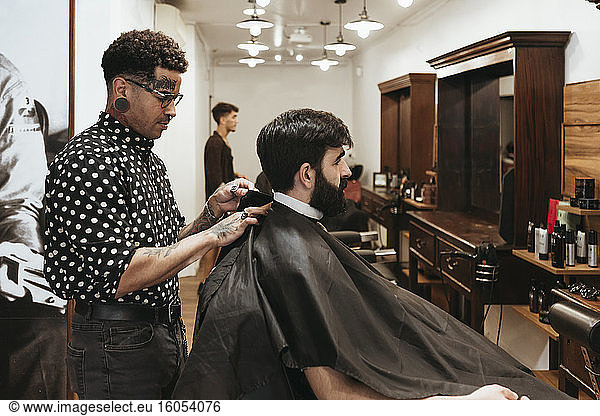 Trendy Friseur Befestigung Umhang auf männlichen Kunden im Salon