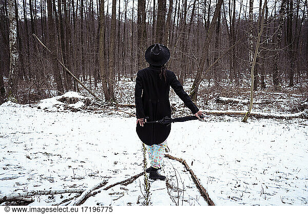 trendy person in black tuxedo balances along snow covered log europe