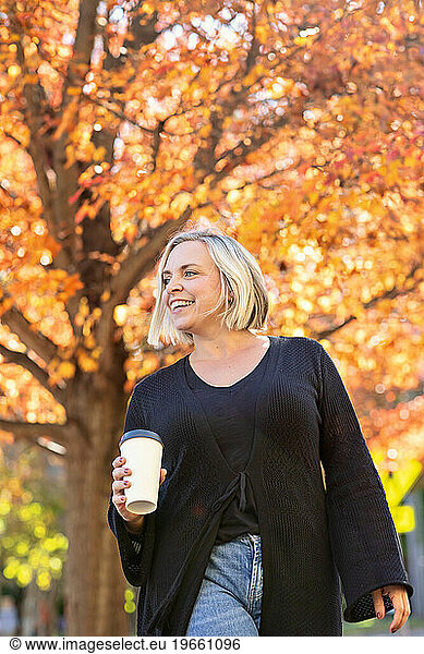 Trendy woman wearing black  holding a coffee cup and walking in autumn