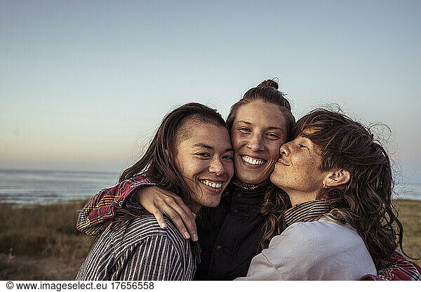 Trio of queer women intimately hug emailing for photo by ocean