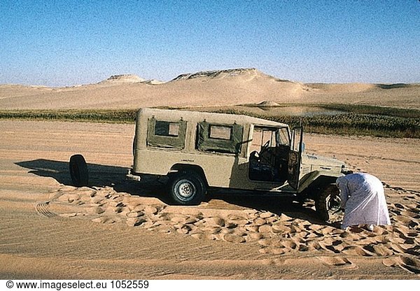 Tuareg changing flat tyre of his 4 wheels drive. Djanet oasis  Sahara desert. Algeria