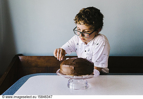 Tween-Boy glasiert seinen Geburtstagskuchen mit Schokoglasur.o