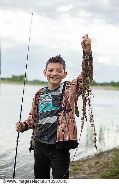 Tween boy holding up seaweed he caught fishing